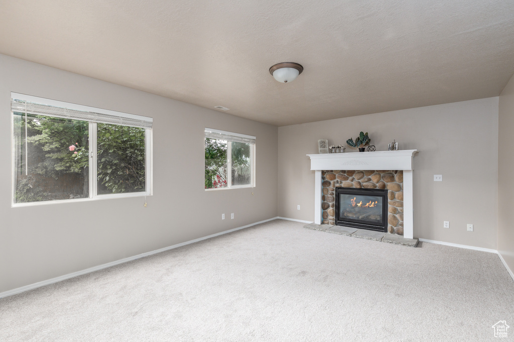 Unfurnished living room featuring carpet floors, baseboards, and a stone fireplace