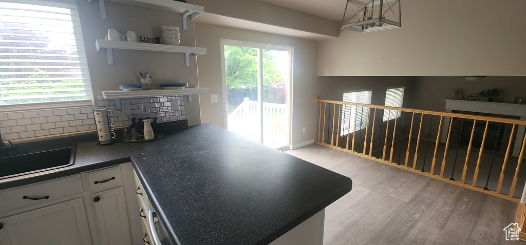Kitchen with light wood-style flooring, white cabinets, open shelves, dark countertops, and tasteful backsplash