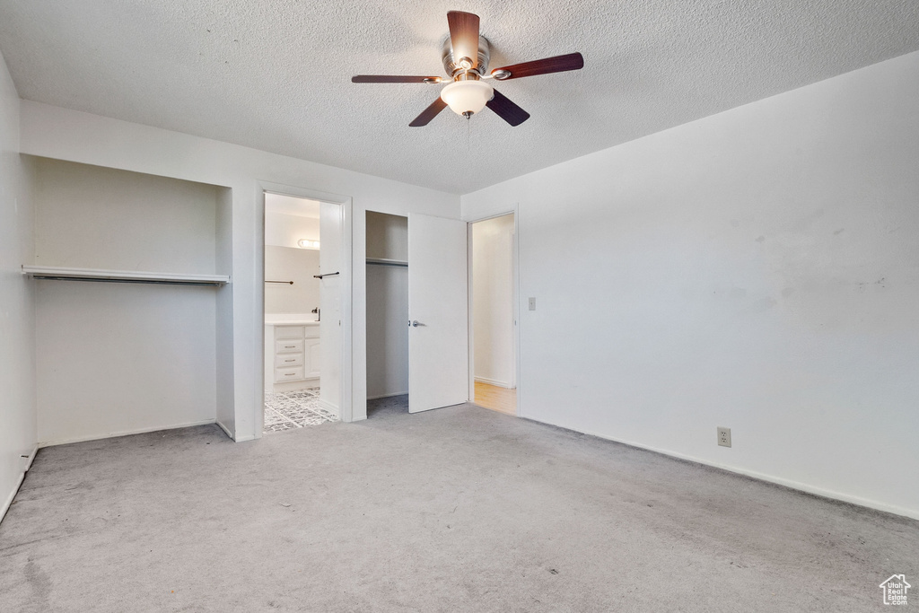 Unfurnished bedroom with a textured ceiling, carpet flooring, ensuite bathroom, and a ceiling fan