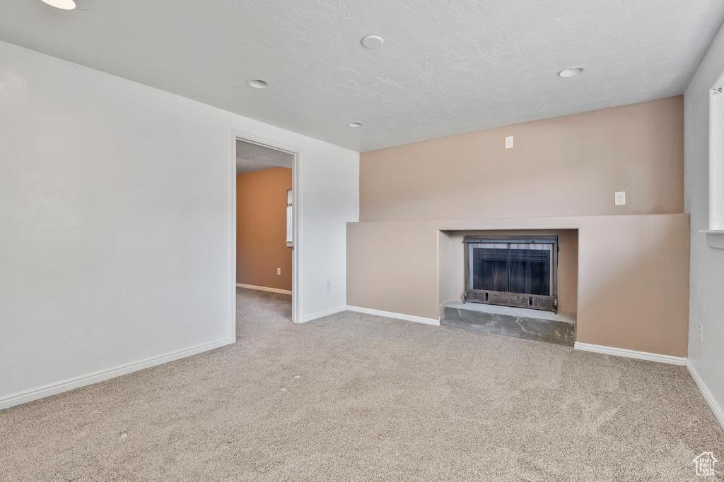 Unfurnished living room featuring baseboards, carpet, recessed lighting, and a fireplace with raised hearth