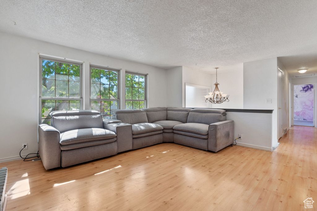 Living area featuring baseboards, a notable chandelier, a textured ceiling, and wood finished floors