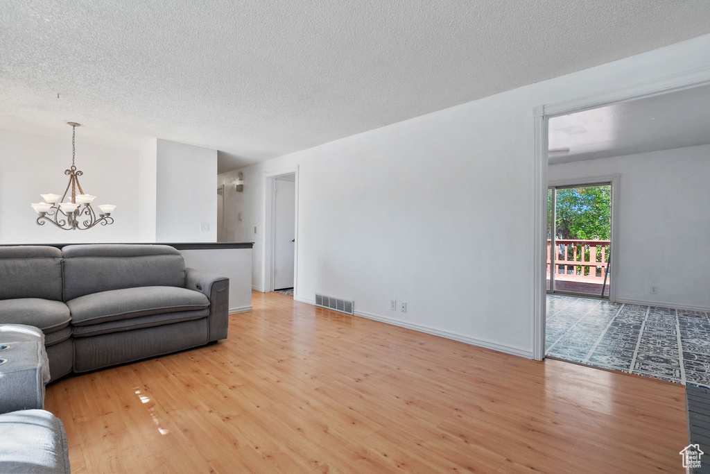 Living area featuring wood finished floors, a notable chandelier, a textured ceiling, visible vents, and baseboards