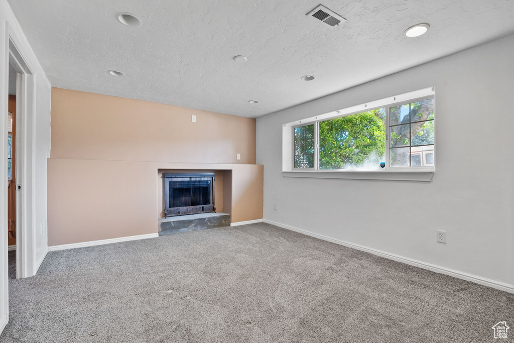 Unfurnished living room with carpet floors, a textured ceiling, visible vents, baseboards, and a fireplace with raised hearth