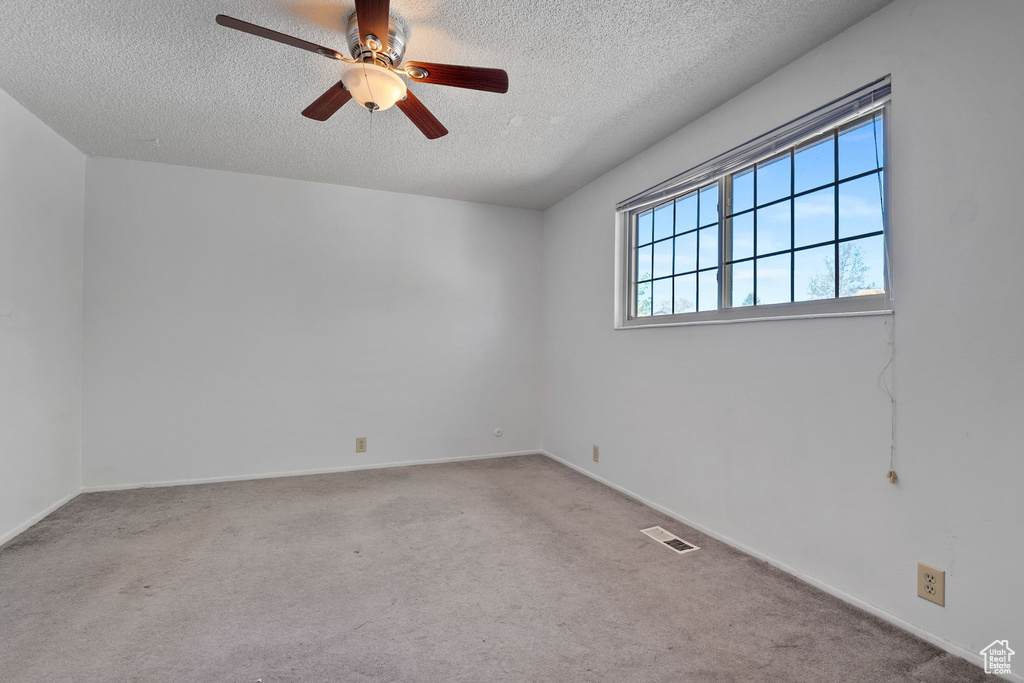 Carpeted empty room with a ceiling fan, baseboards, visible vents, and a textured ceiling