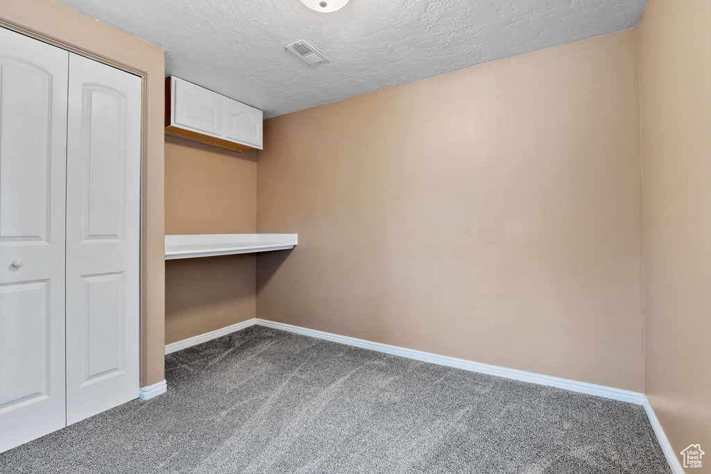 Interior space featuring baseboards, dark colored carpet, visible vents, and a textured ceiling