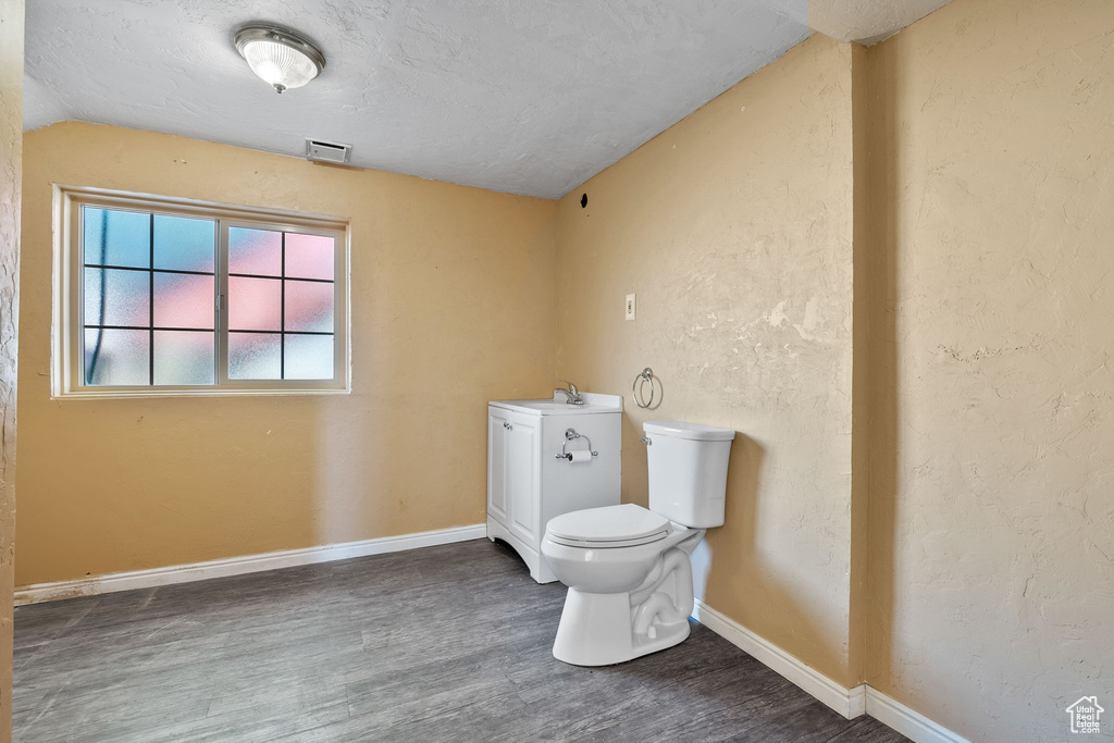 Half bath with toilet, baseboards, visible vents, and wood finished floors