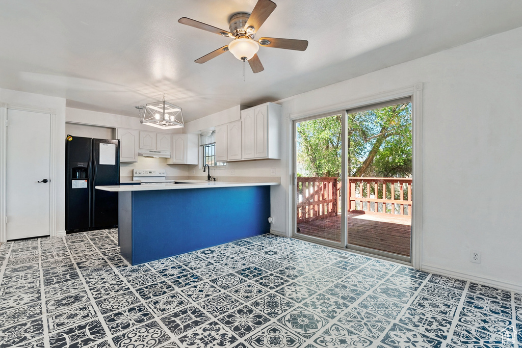 Kitchen featuring under cabinet range hood, electric range oven, a wealth of natural light, black fridge, and a peninsula