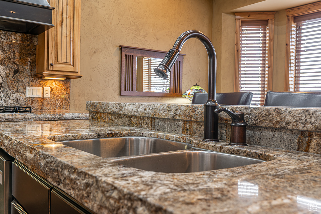 Details featuring a sink, a textured wall, backsplash, and custom range hood