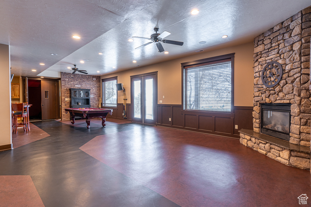 Playroom featuring a wainscoted wall, pool table, ceiling fan, finished concrete flooring, and a stone fireplace