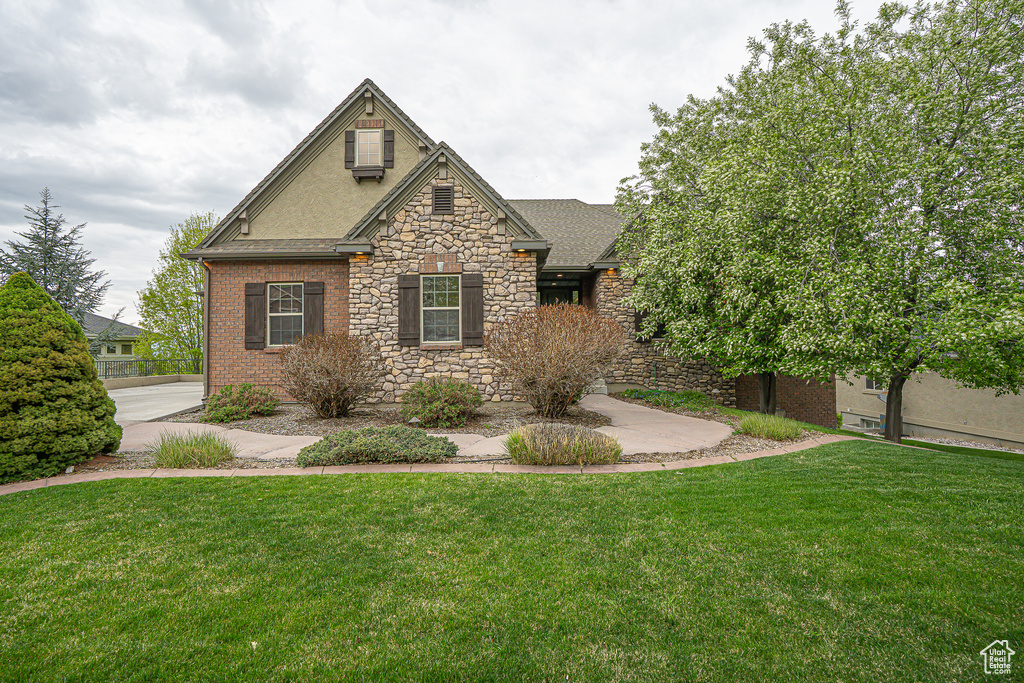 View of front of property with stone siding, roof with shingles, and a front lawn