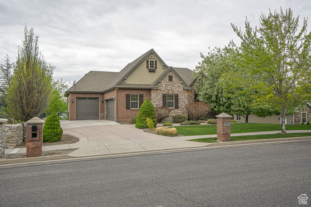 View of front of home featuring stone siding, a garage, roof with shingles, a front yard, and driveway