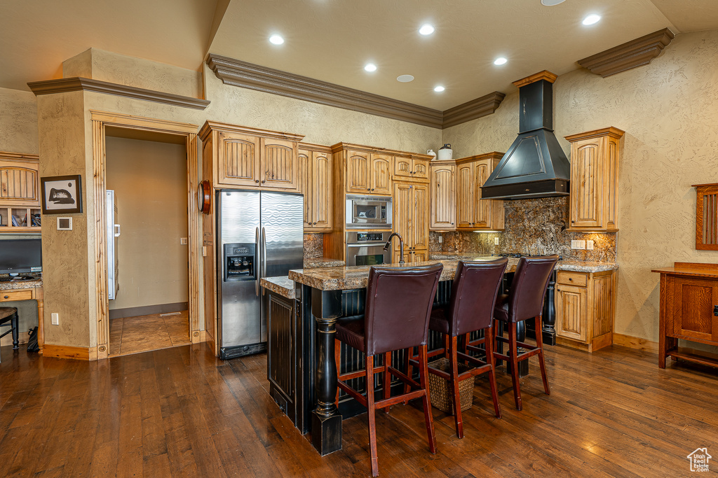 Kitchen with premium range hood, dark wood finished floors, a center island with sink, baseboards, and appliances with stainless steel finishes