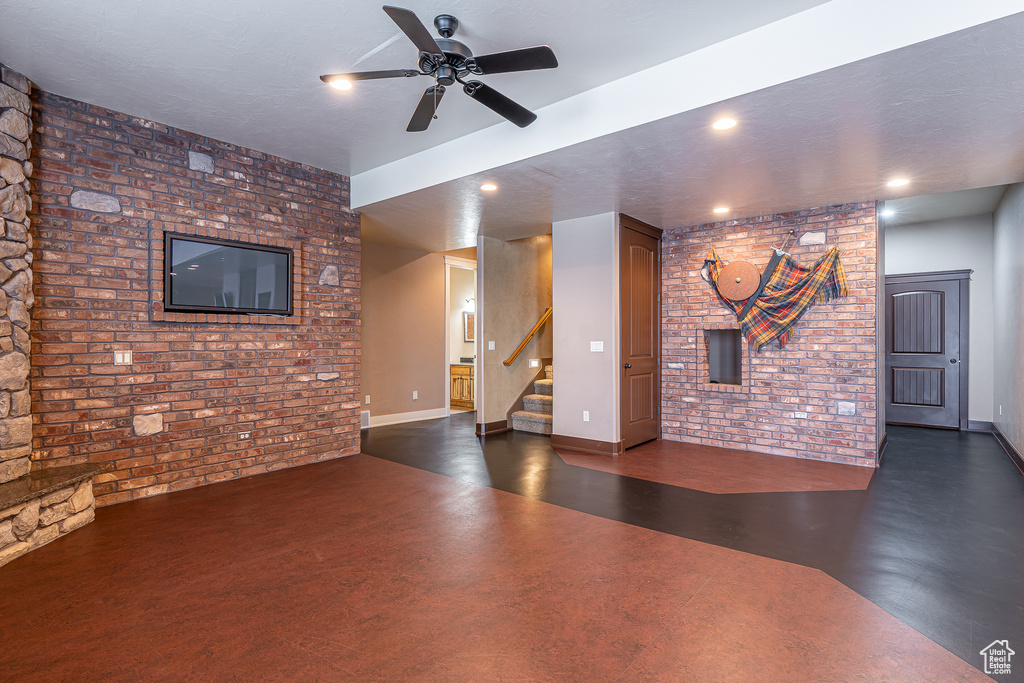 Unfurnished living room featuring stairway, ceiling fan, finished concrete floors, and brick wall
