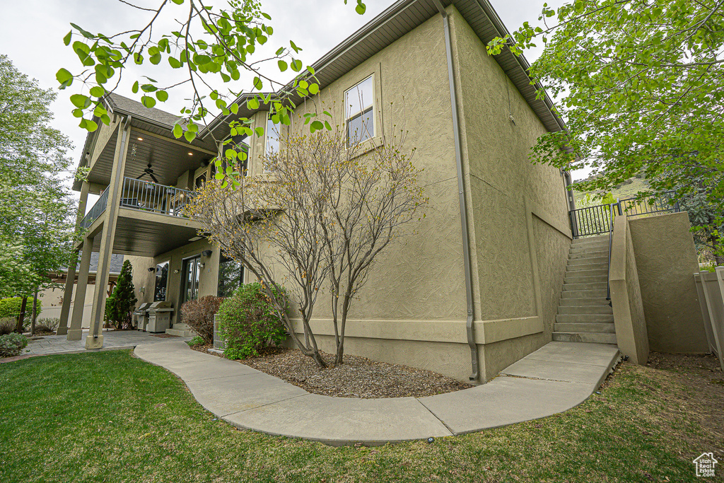 Back of property featuring stairs, a balcony, stucco siding, ceiling fan, and a lawn