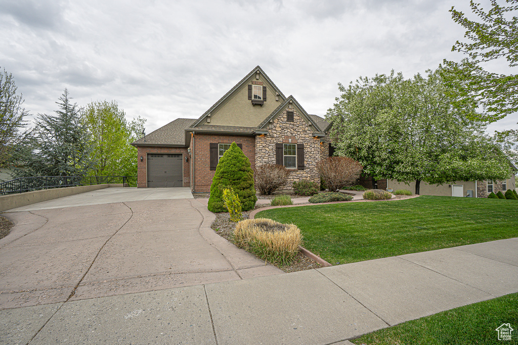 View of front of property featuring driveway, brick siding, a front yard, a garage, and stone siding
