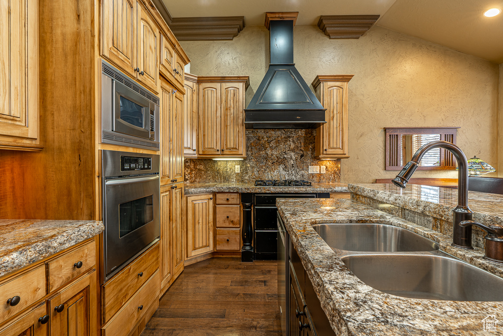 Kitchen featuring a sink, stainless steel appliances, a textured wall, custom exhaust hood, and dark wood-style floors