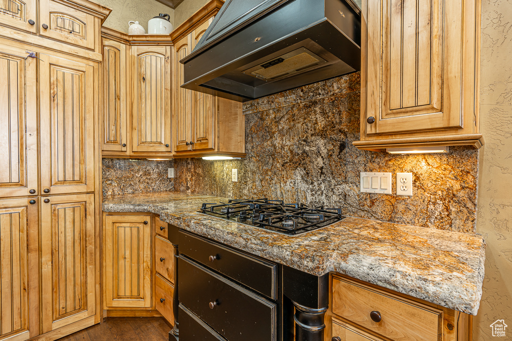 Kitchen featuring under cabinet range hood, decorative backsplash, light stone counters, and black gas cooktop
