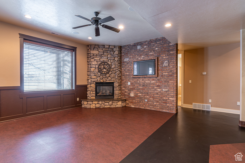 Unfurnished living room with a wainscoted wall, visible vents, a ceiling fan, and a stone fireplace