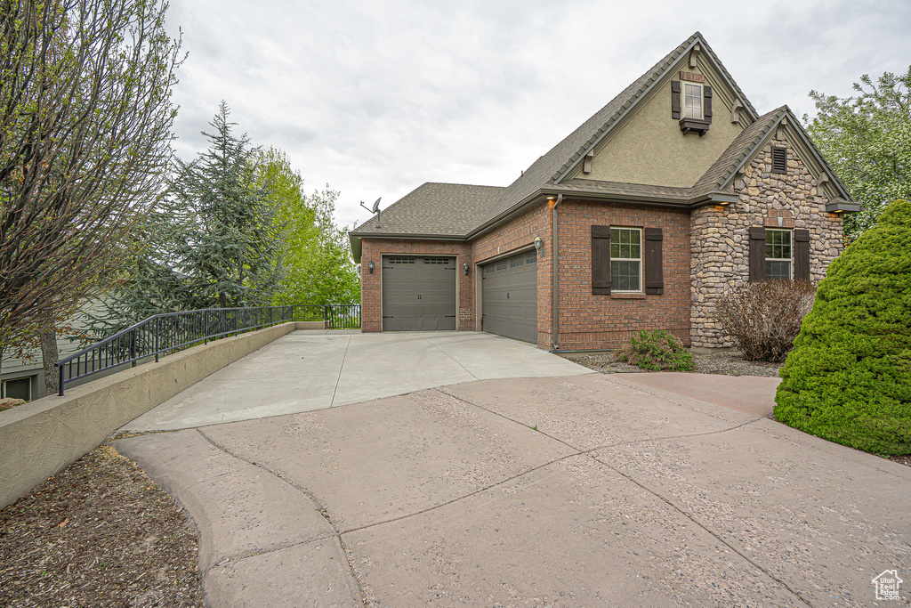 View of home's exterior featuring an attached garage, fence, roof with shingles, brick siding, and driveway