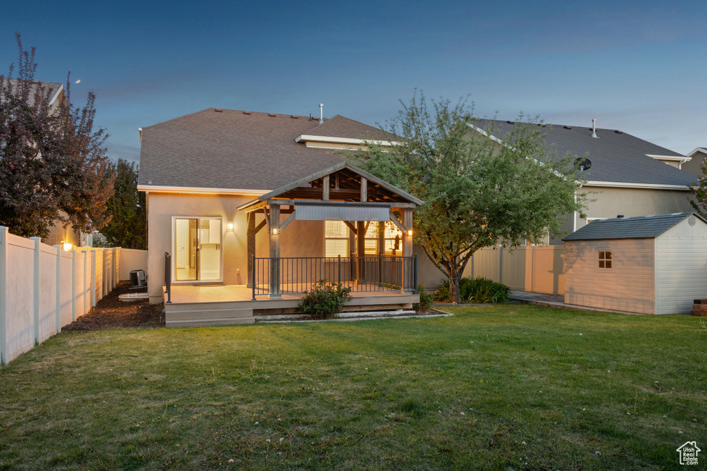 Back of house with a deck, a fenced backyard, a storage unit, a gazebo, and an outbuilding