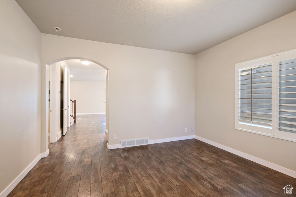 Unfurnished room featuring arched walkways, baseboards, visible vents, and dark wood-type flooring