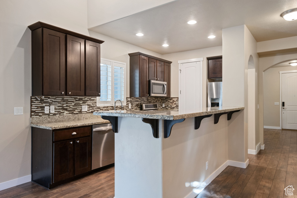 Kitchen with a breakfast bar area, dark brown cabinets, appliances with stainless steel finishes, and decorative backsplash