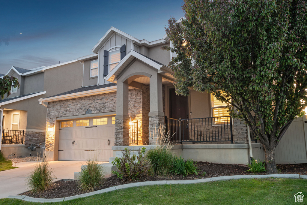 View of front of house with covered porch, driveway, stone siding, and stucco siding