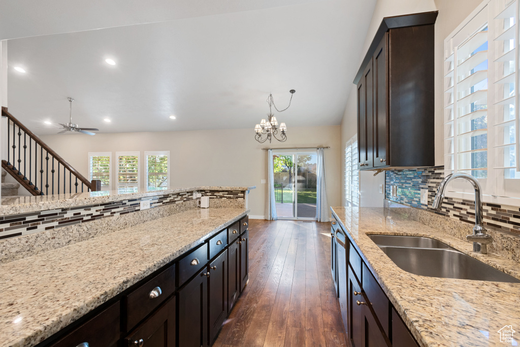 Kitchen with a sink, light stone counters, decorative backsplash, and dark wood finished floors
