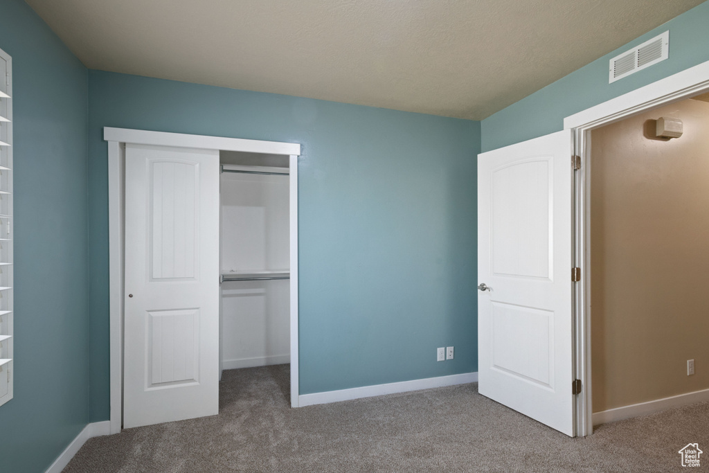 Unfurnished bedroom with carpet floors, baseboards, visible vents, and a closet