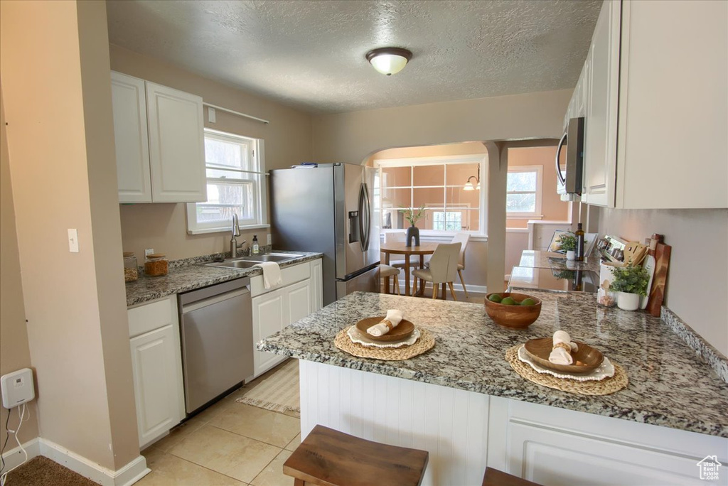 Kitchen with stainless steel appliances, a sink, a peninsula, white cabinetry, and arched walkways