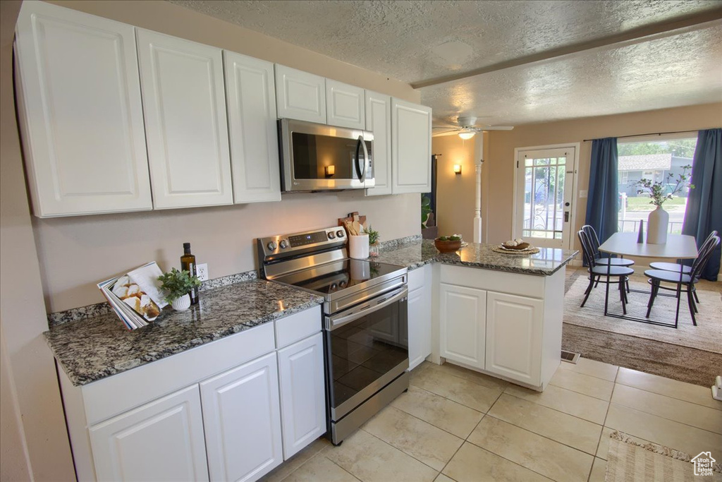 Kitchen with appliances with stainless steel finishes, a peninsula, a textured ceiling, white cabinetry, and a ceiling fan