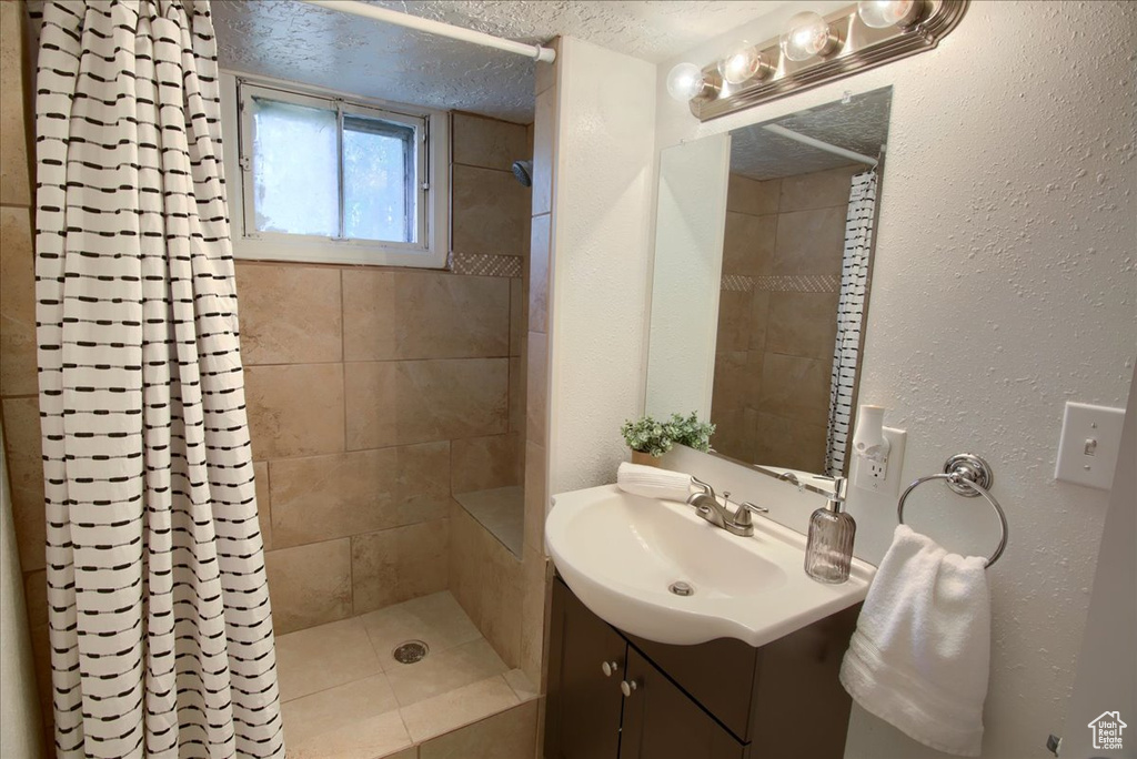 Bathroom featuring a tile shower, vanity, a textured ceiling, and a textured wall