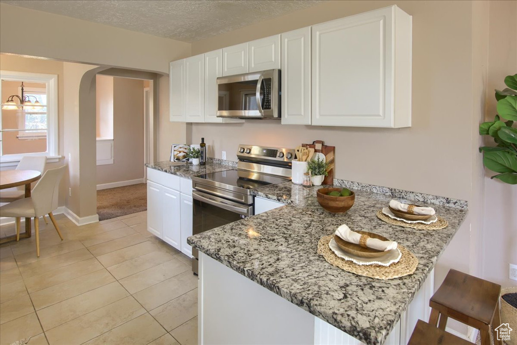 Kitchen featuring stainless steel appliances, a peninsula, white cabinets, light stone countertops, and arched walkways