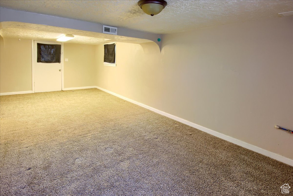 Finished basement featuring a textured ceiling, carpet floors, and baseboards