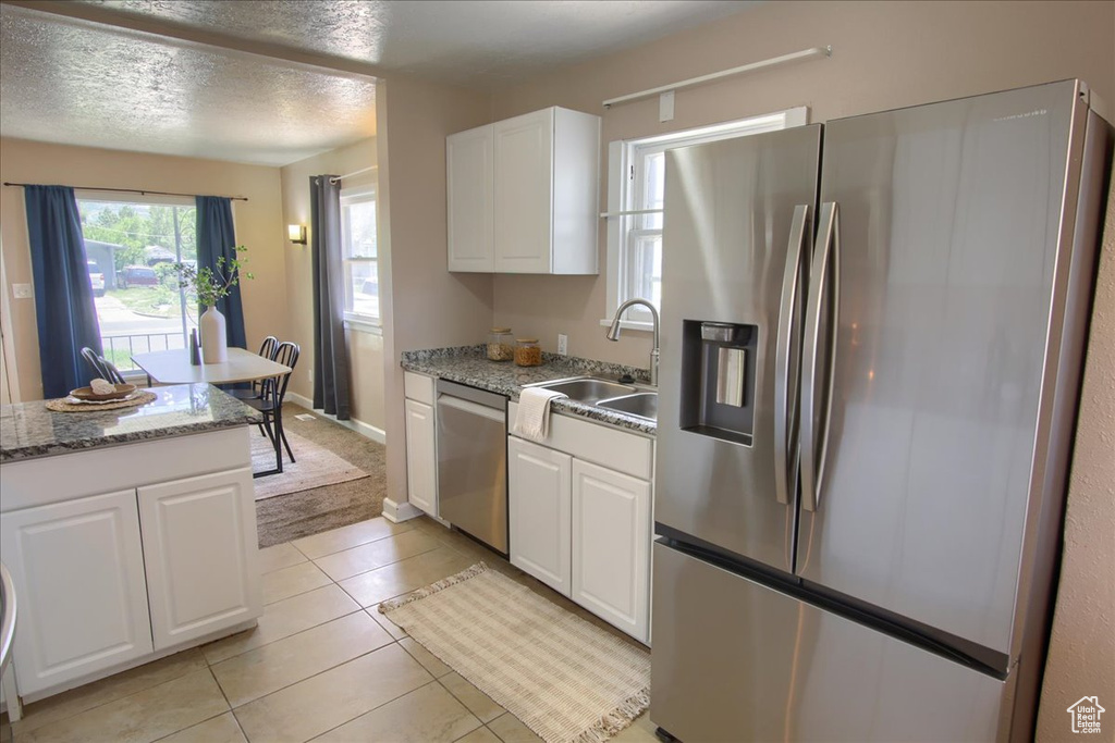 Kitchen featuring stainless steel appliances, white cabinets, a sink, light tile patterned floors, and a textured ceiling