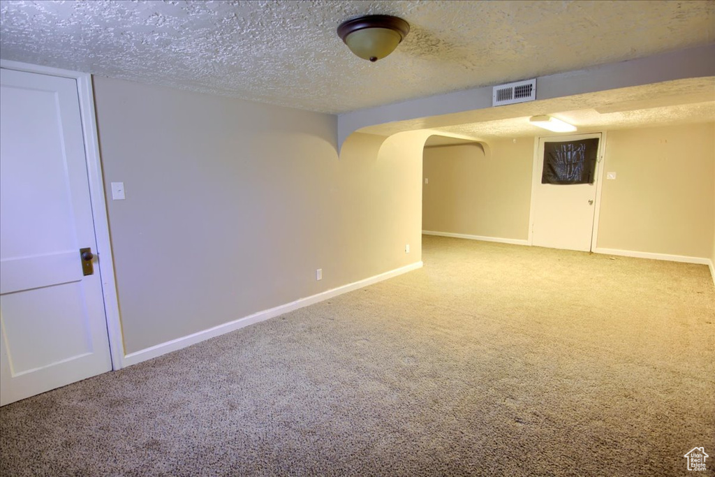 Spare room with carpet flooring, baseboards, a textured ceiling, and arched walkways