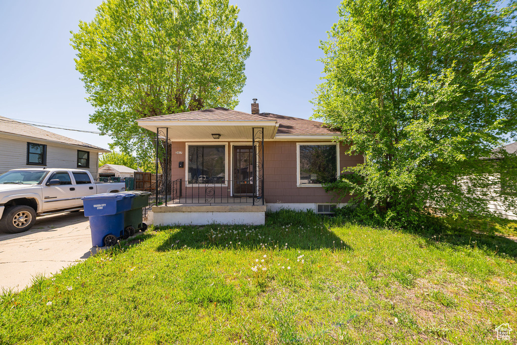 Bungalow-style house with a shingled roof, covered porch, a chimney, and a front yard