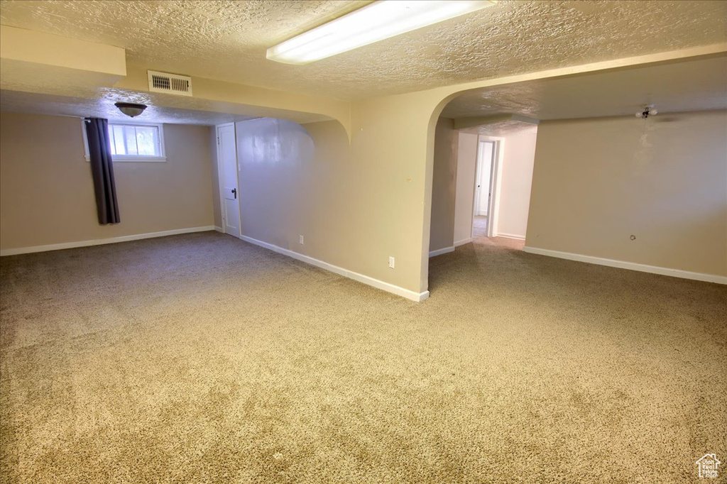 Carpeted spare room featuring a textured ceiling, baseboards, and arched walkways