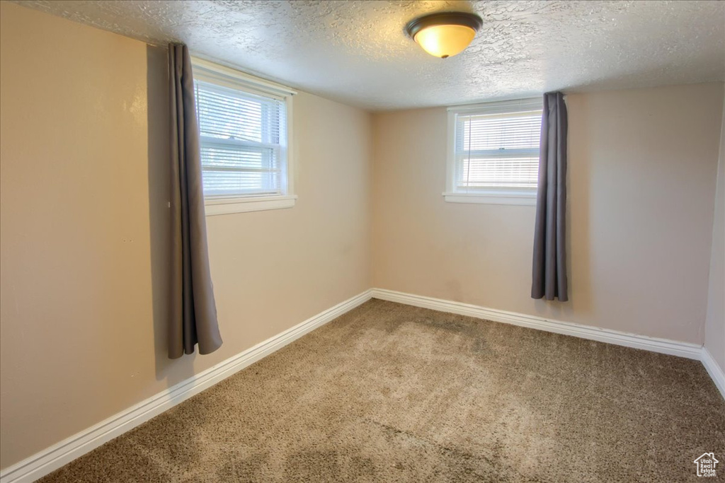 Carpeted empty room featuring a textured ceiling, baseboards, and healthy amount of natural light
