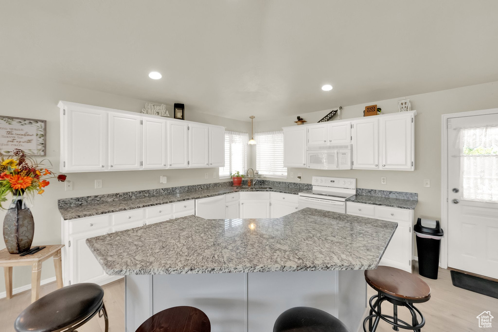 Kitchen featuring a sink, a breakfast bar, light stone counters, white appliances, and white cabinets