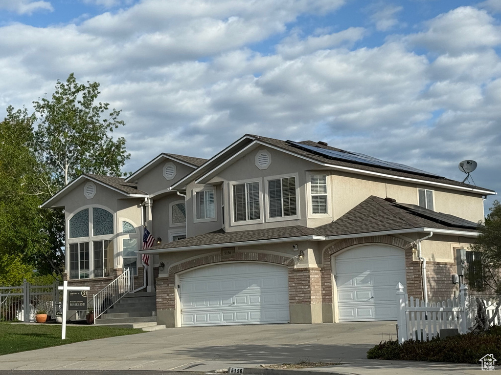 View of front of home featuring fence, stucco siding, an attached garage, driveway, and solar panels