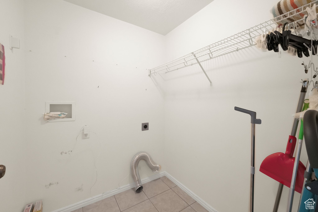 Clothes washing area with light tile patterned floors, laundry area, electric dryer hookup, hookup for a washing machine, and baseboards