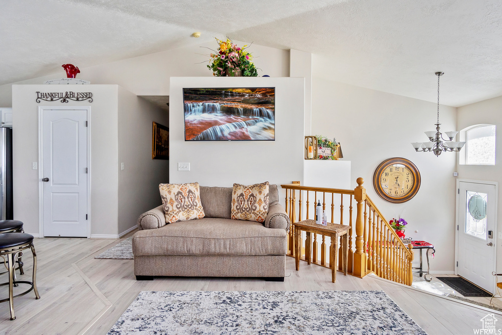 Living room featuring a chandelier, baseboards, light wood finished floors, and lofted ceiling