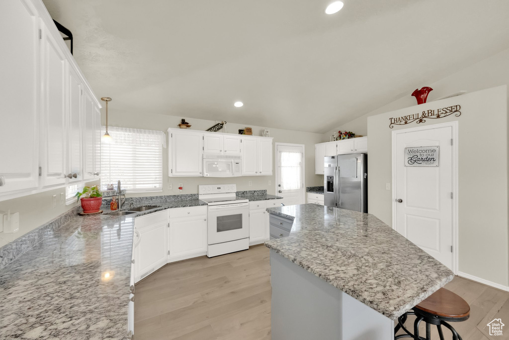 Kitchen with light stone countertops, light wood-style floors, white appliances, and a kitchen island