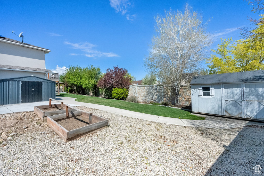 View of yard featuring fence, a storage unit, a garden, and an outbuilding
