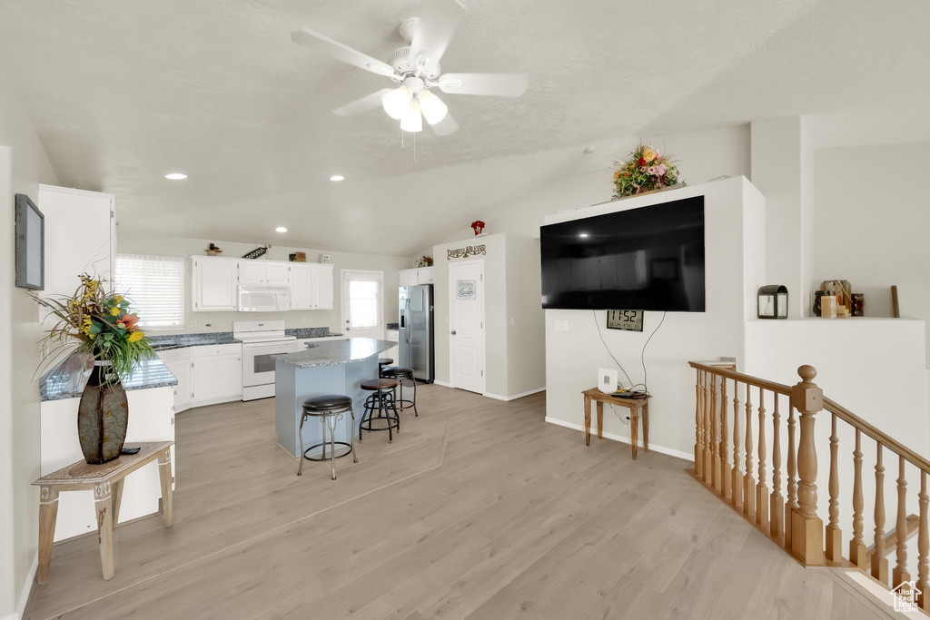 Interior space with white appliances, a breakfast bar area, white cabinets, a center island, and a ceiling fan