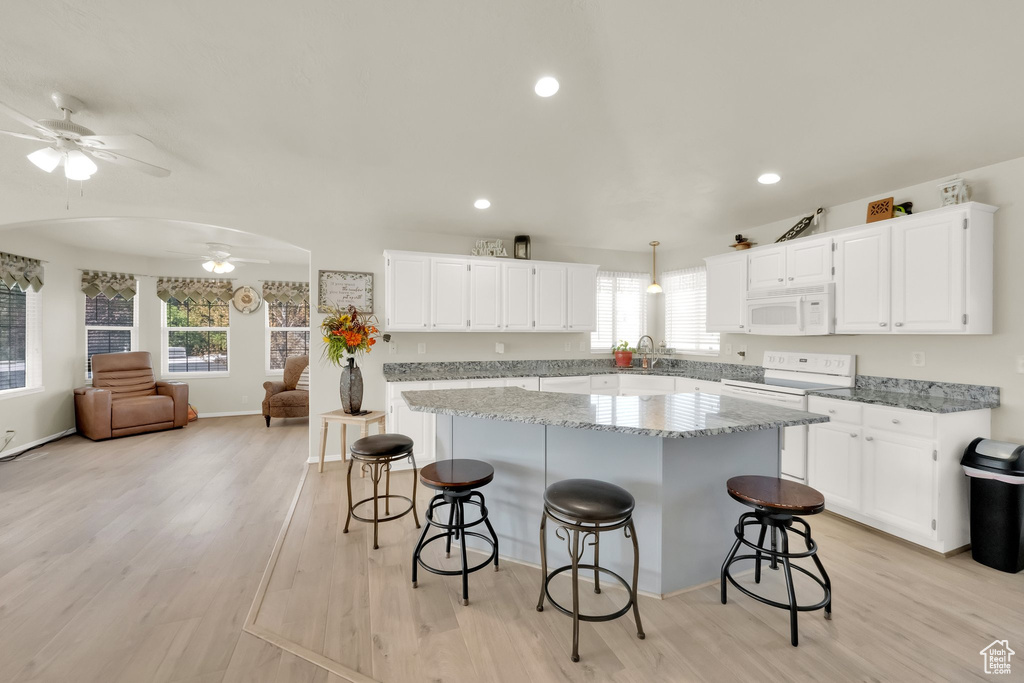 Kitchen featuring light wood-style floors, a center island, open floor plan, white appliances, and a ceiling fan