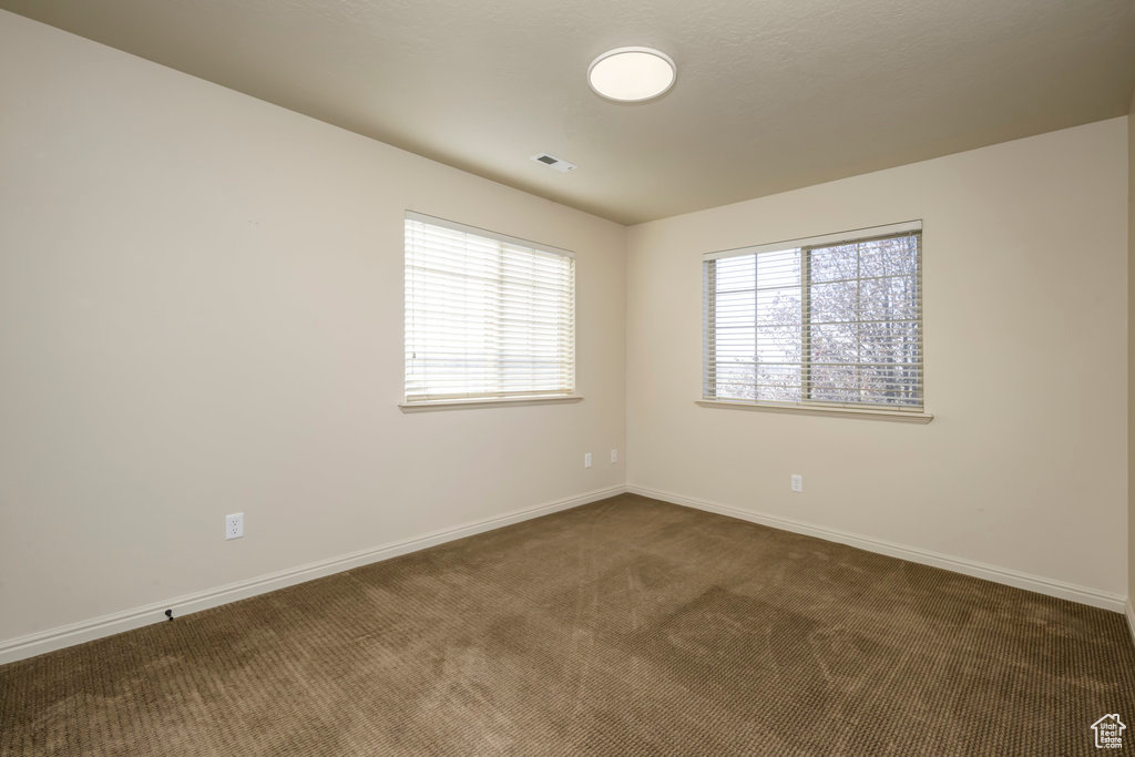 Unfurnished room with visible vents, baseboards, and dark carpet