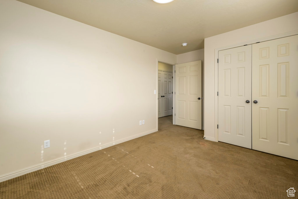 Unfurnished bedroom with a closet, light carpet, and baseboards
