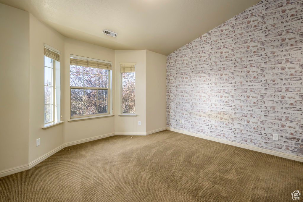 Carpeted empty room with vaulted ceiling, baseboards, and visible vents